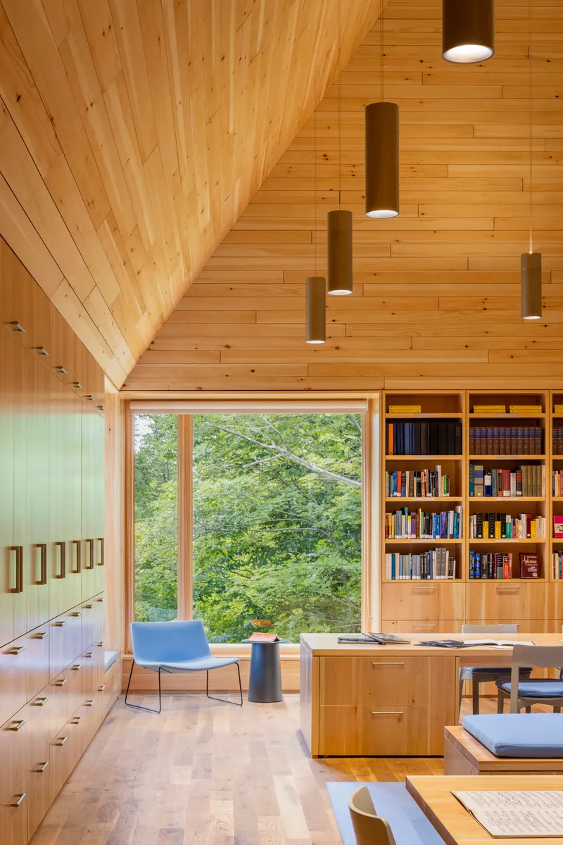 Library corner with built-in bookshelves, reading table, and large window facing the forested hillside