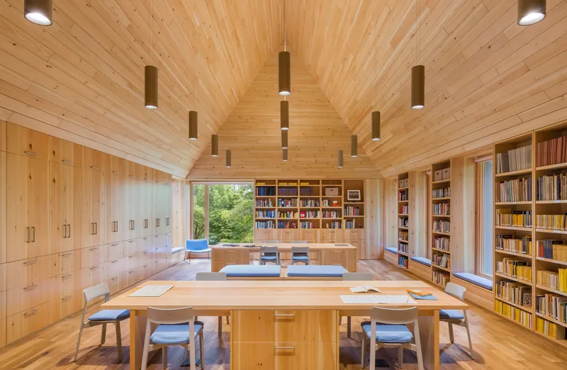 Wide view of the library with reading tables, built-in shelving, and a vaulted timber ceiling