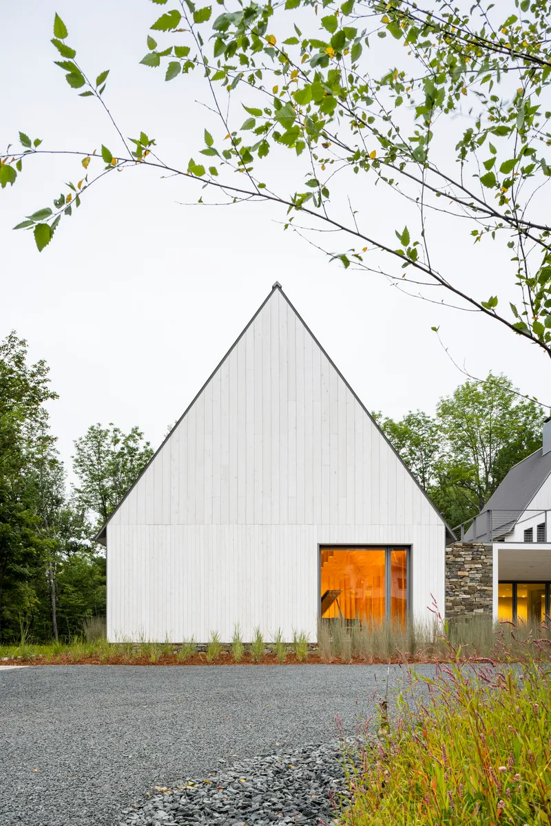 Tall gable facade with warm-lit timber entry and overhanging birch branches at dusk