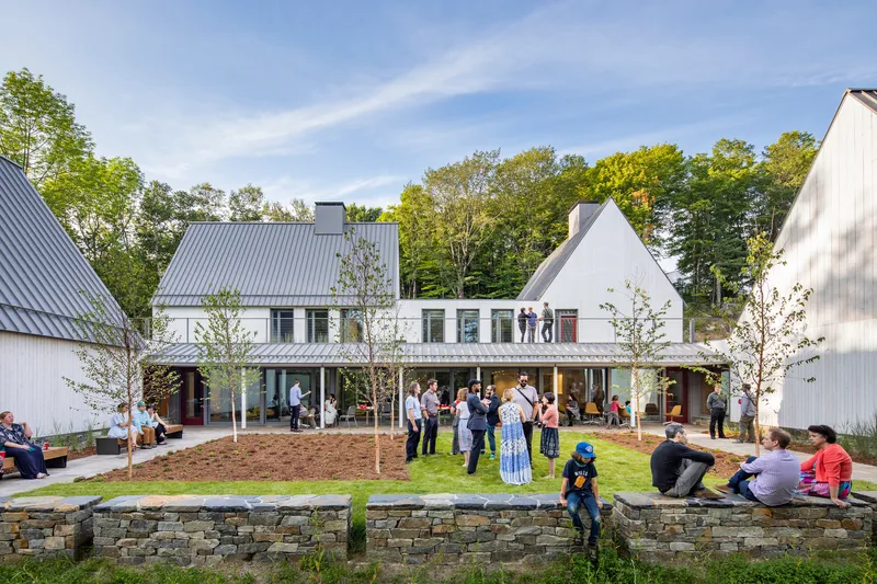 White gabled buildings around a lawn with visitors gathering on an afternoon under blue sky