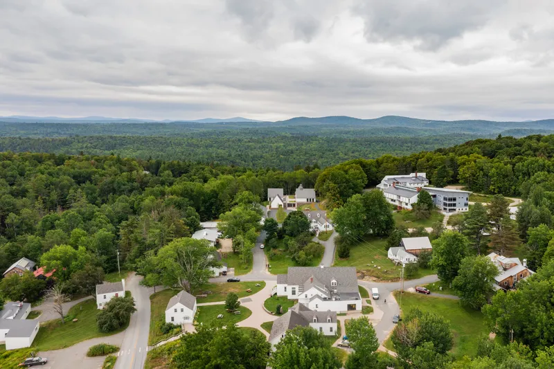 Aerial view of white gabled buildings arranged around curved roads within a forested valley