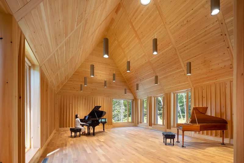 Interior of a timber-lined rehearsal hall with vaulted ceiling and pendant lights above two grand pianos