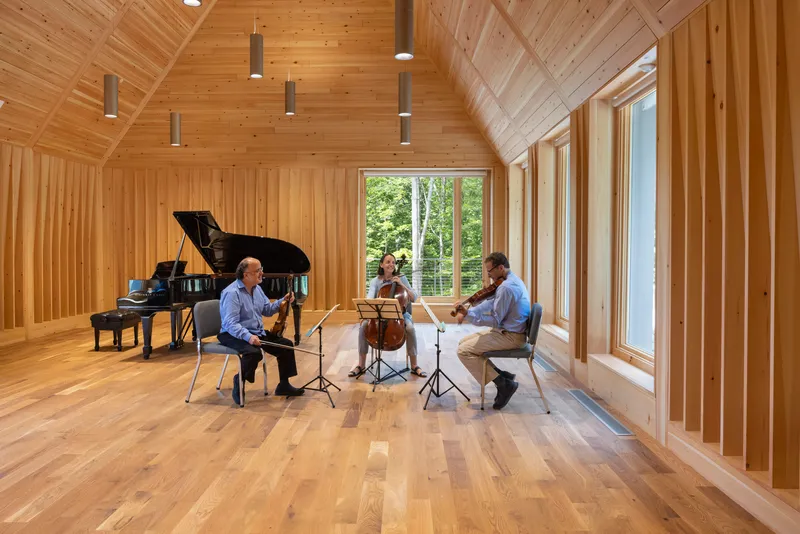 Musicians performing in the timber-paneled room with tall windows overlooking trees