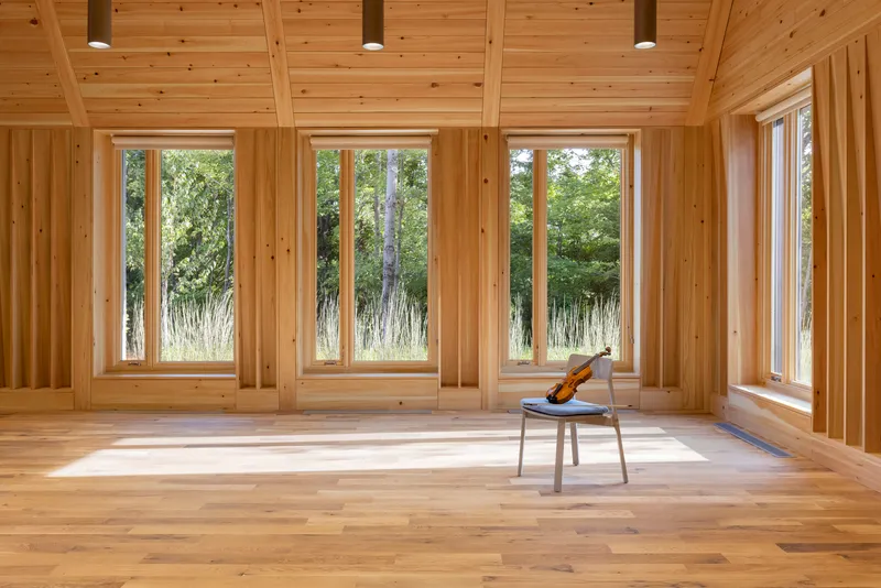 Empty timber-framed room with four tall windows, single chair with violin, and afternoon sunlight across the floor