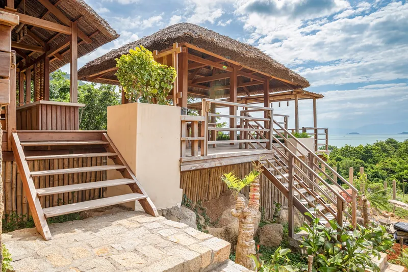 Timber staircase connecting elevated pavilions with thatched roofs and horizontal bamboo cladding