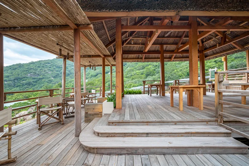 Open timber terrace with exposed thatched roof structure overlooking forested hillside