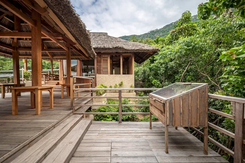Wooden deck railing and terraced steps leading toward a thatched roof pavilion with green hillside backdrop