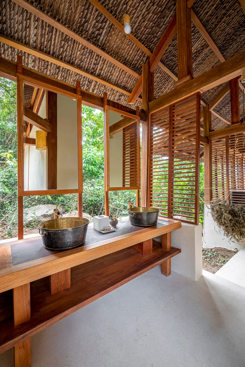 Bathroom with timber vanity, stone vessel sinks and louvered screens opening to garden vegetation