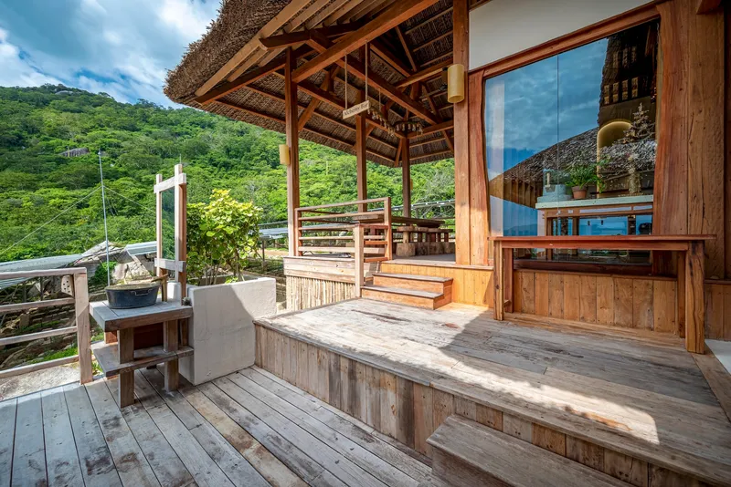 Corner deck platform with timber bench seating under thatched eaves and mountain view