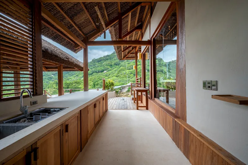 Kitchen counter with timber cabinetry and concrete floor opening to covered deck with valley view