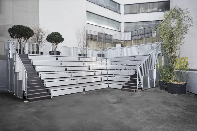 Metal bleacher seating with planted trees in containers on an outdoor courtyard terrace