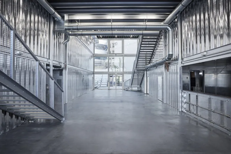 Interior view showing metal staircases, exposed structural beams, and corrugated wall panels in natural light