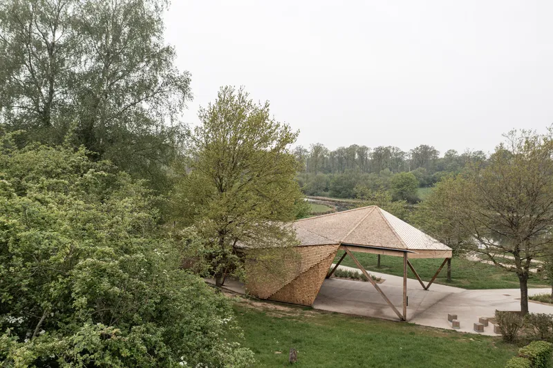 Elevated view of the timber pavilion with woven lattice facade set among trees in a park