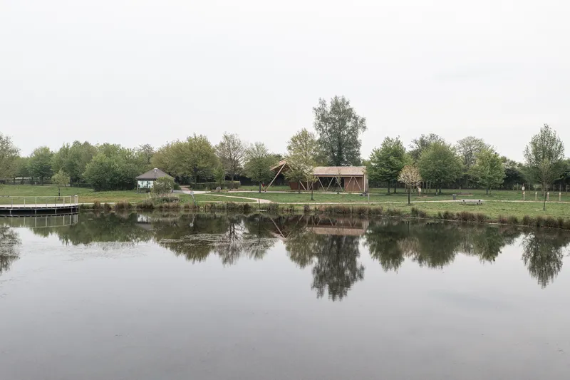 Timber pavilion reflected in the still pond surface with trees lining the grassy shore