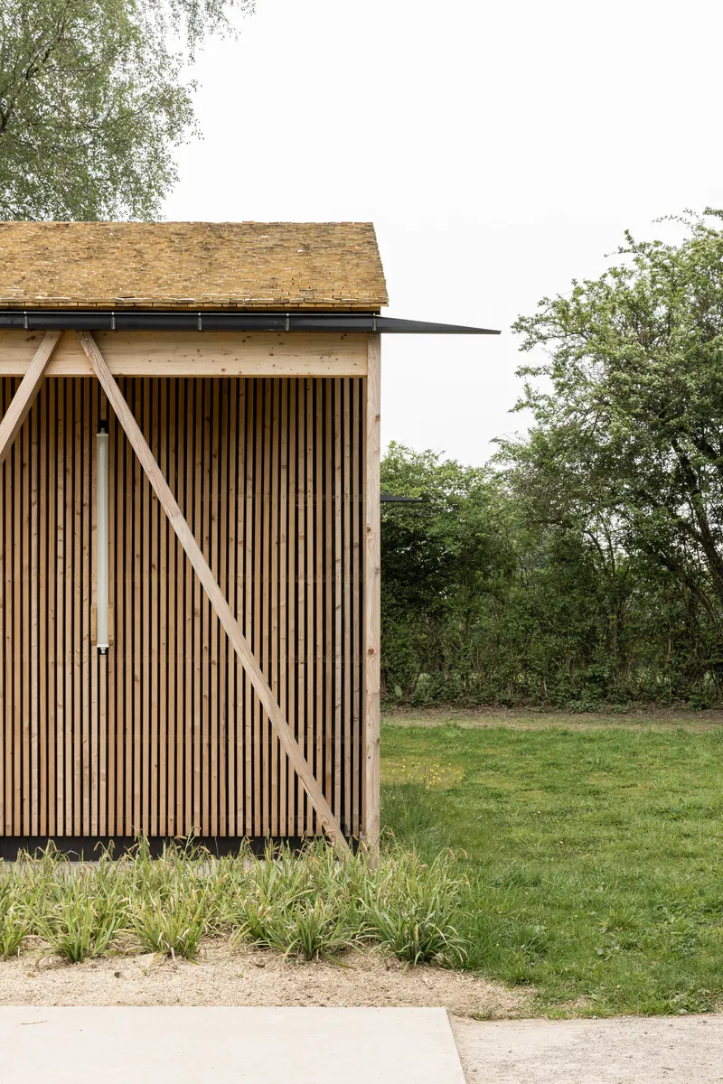 Vertical wood slat wall with diagonal timber brace below a shallow pitched shingle roof