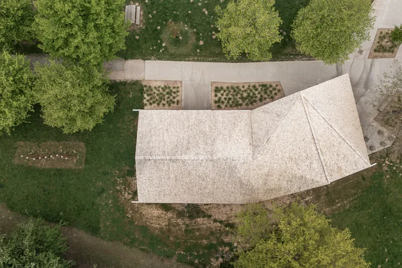 Aerial view of shingled roof with planted beds and pathways arranged around the pavilion structure