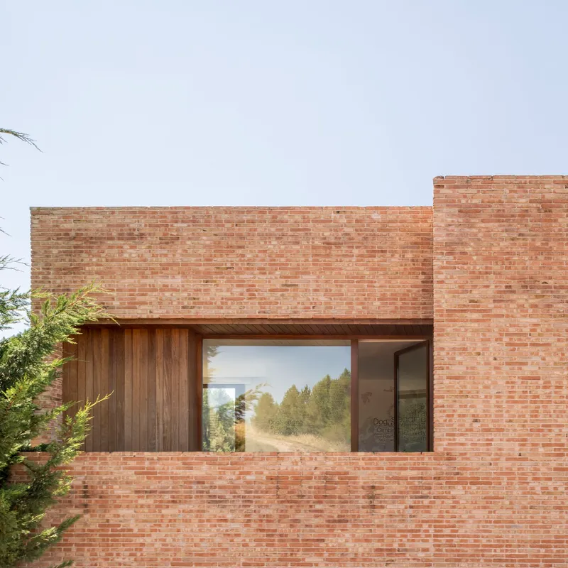 Horizontal window set into a brick facade with timber cladding beneath an overcast sky