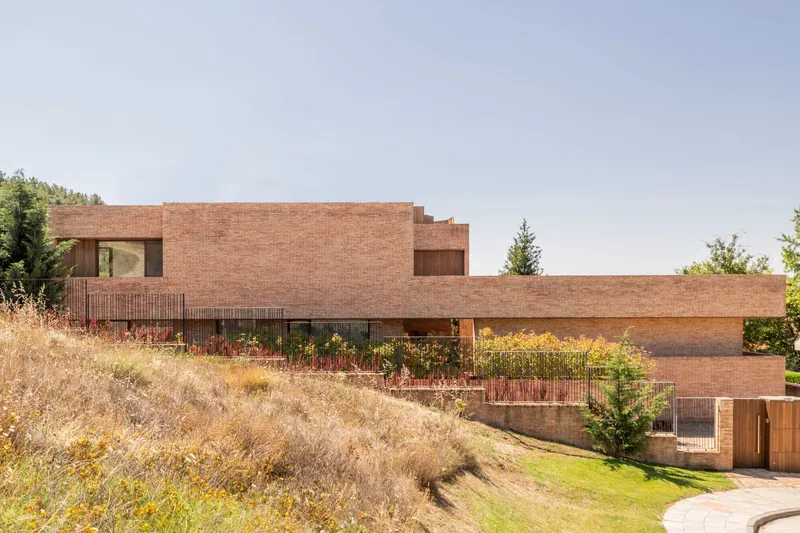 Stepped brick facade with planted terraces descending a sloped site with dry grasses