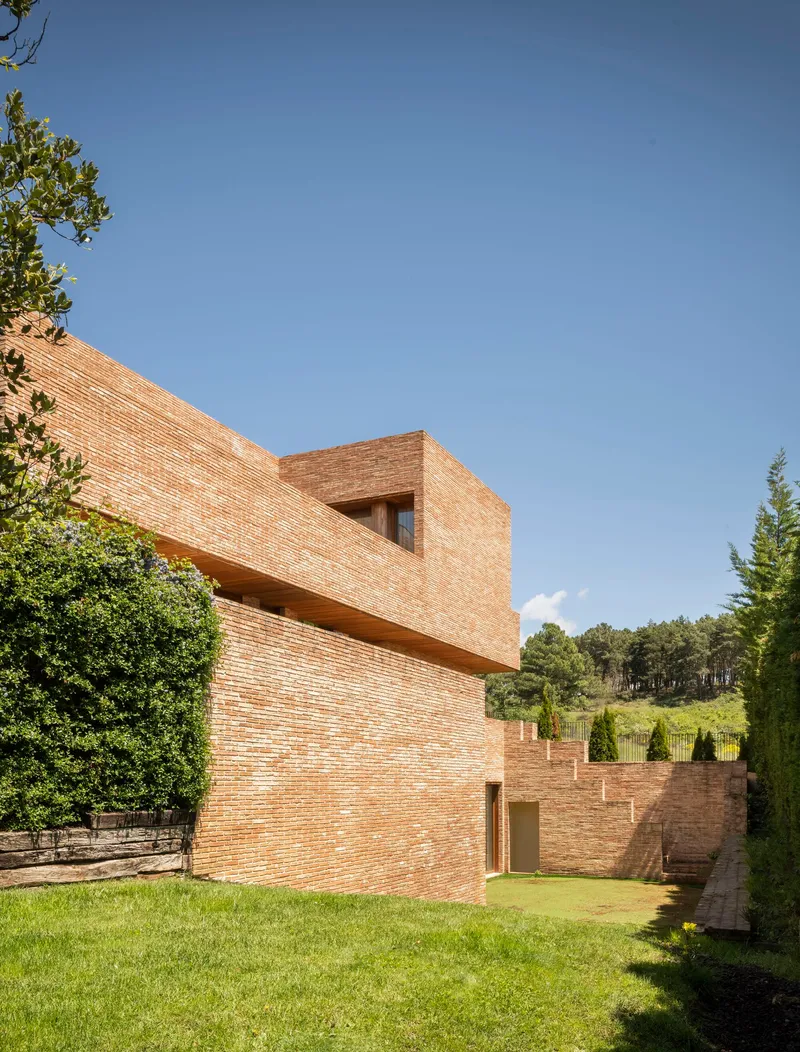 Stacked brick volumes with a terrace opening framed by a lawn and surrounding trees