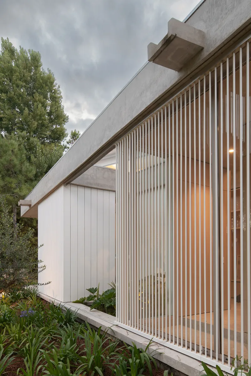 Angled concrete beam over vertical timber slat screen and white cladding beneath an overcast sky