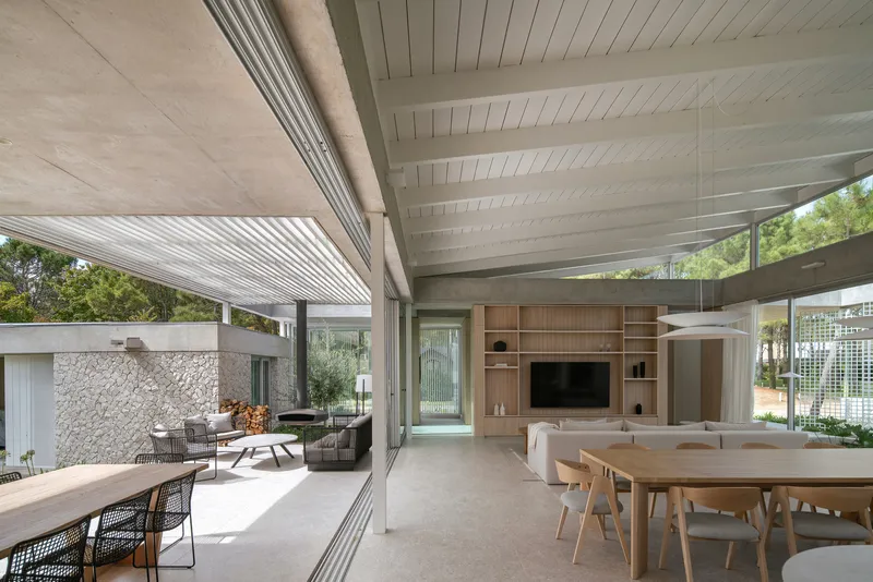 Living and dining area with exposed concrete beams and floor-to-ceiling glass opening to covered terrace