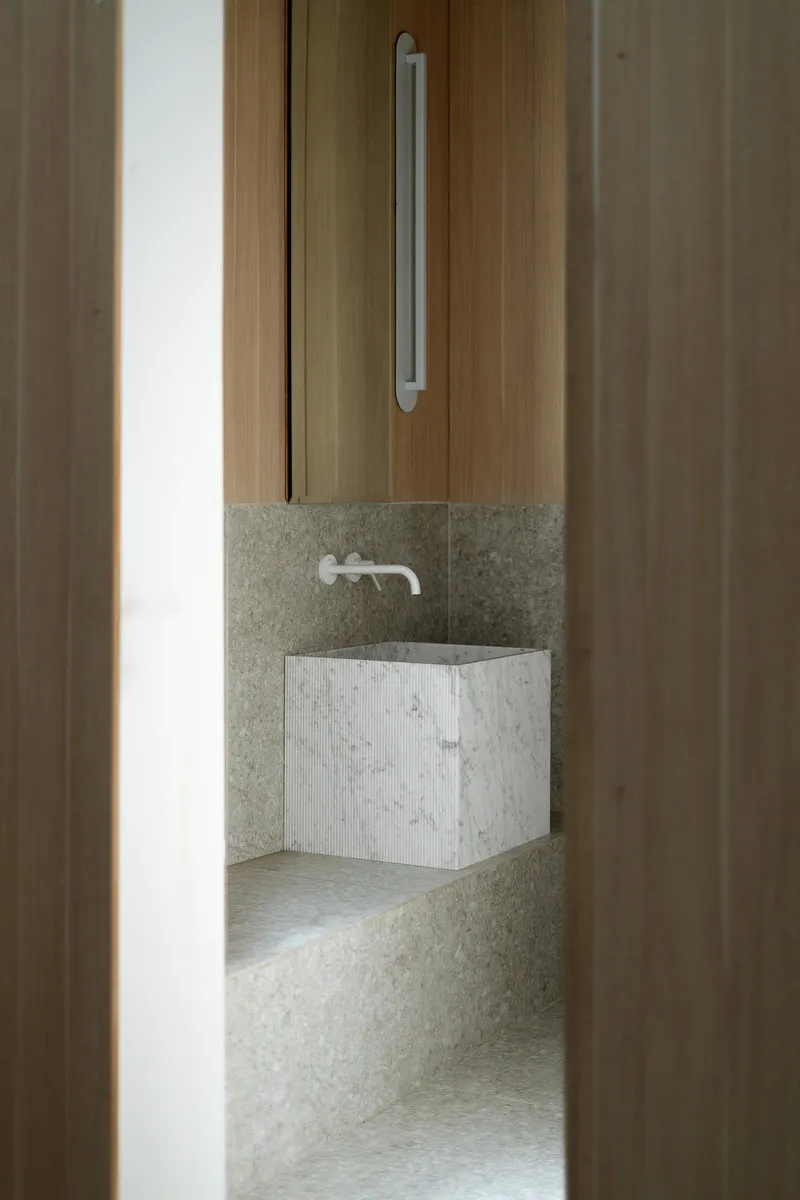 View through timber door of a textured stone bathroom with wall-mounted sink and integrated basin