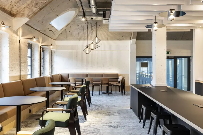 Café interior with tan banquettes, exposed concrete vaults, and pendant lights above round tables