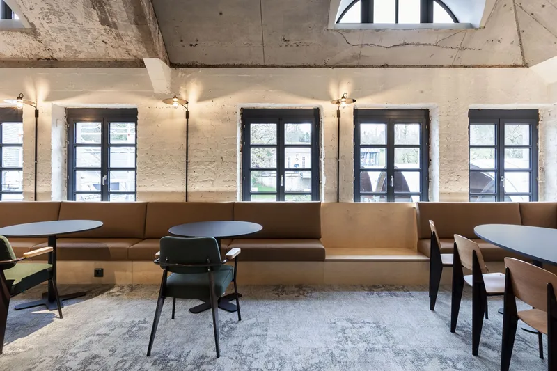 Seating area with continuous tan upholstered benches below a row of dark steel-framed windows