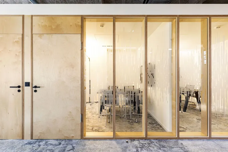 Corridor view through glazed timber screens revealing a meeting room with polished concrete floor