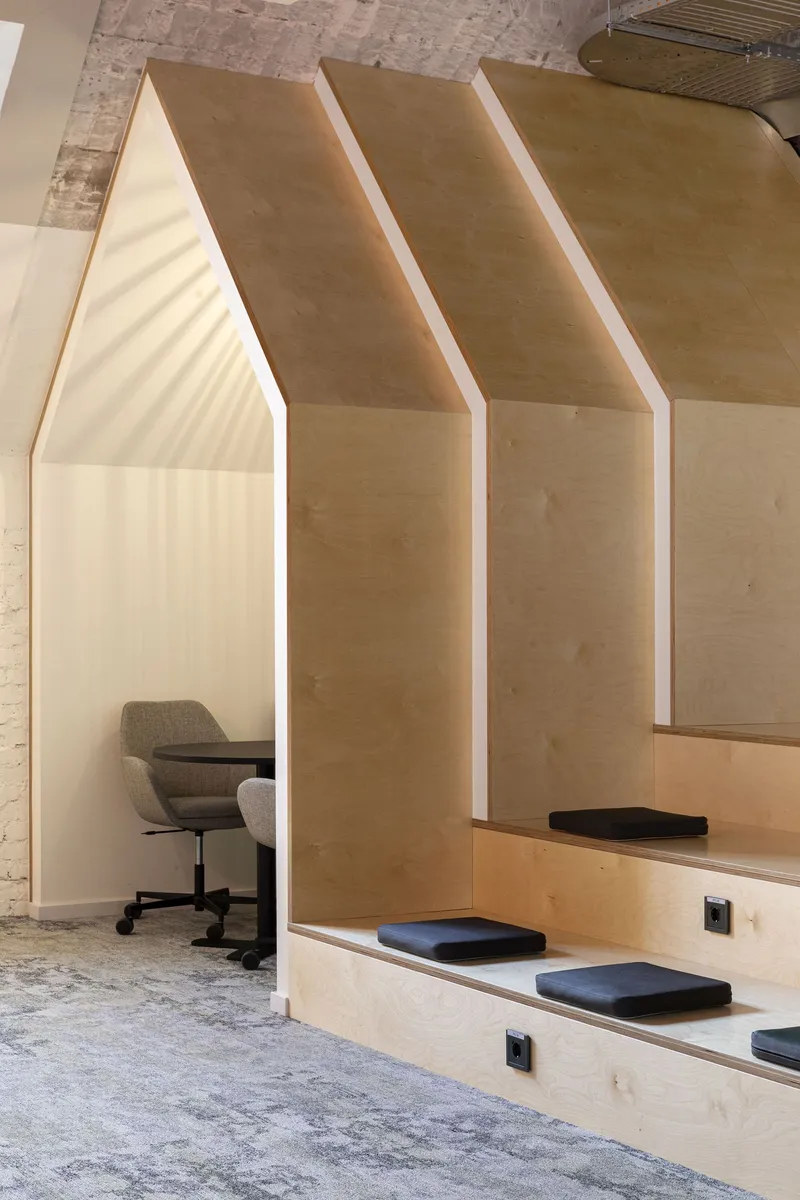 Plywood alcoves with peaked tops framing individual workstations and cushioned bench seating