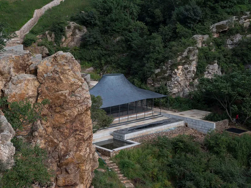 Aerial view of the glazed pavilion with curved metal roof nestled between limestone cliffs and vegetation