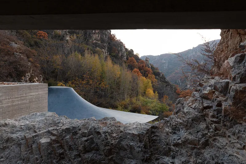 View from beneath concrete overhang toward the curved roof canopy and autumn hillside beyond rock formations