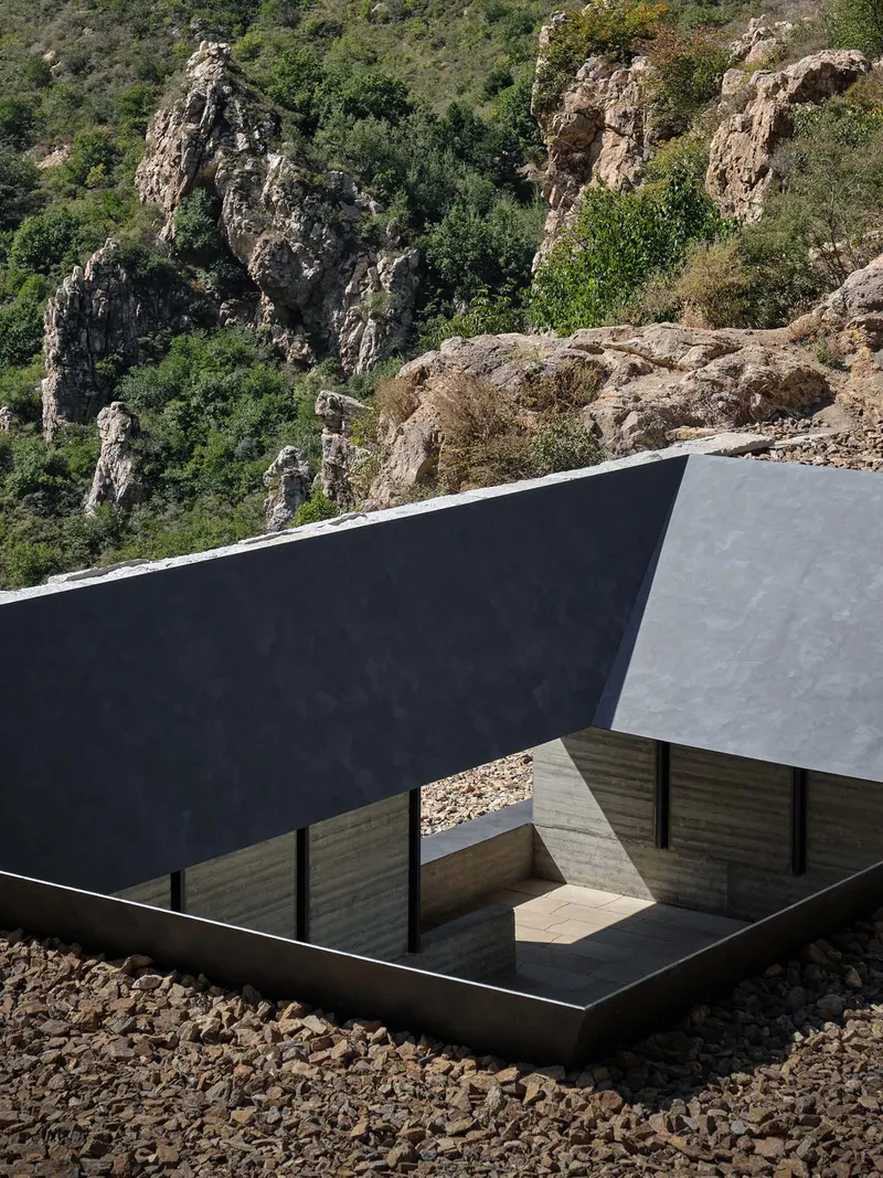 Aerial view of the sunken courtyard with dark metal roof planes set into the rocky hillside