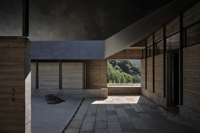 Interior courtyard with rammed earth walls, dark paving and a single boulder under filtered daylight