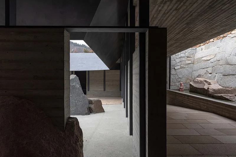View through steel frame doorway into passage with boulders and stacked stone wall beyond