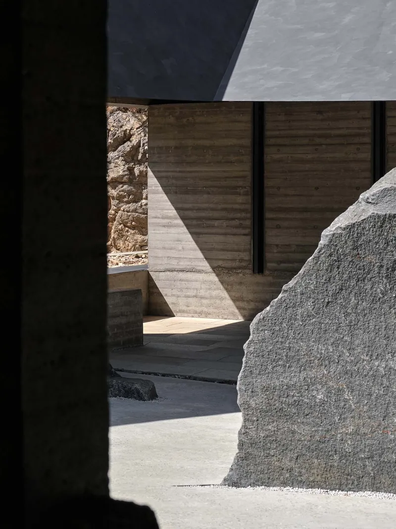 Sunlit courtyard corner framed by shadow with boulder and timber formwork wall in bright light