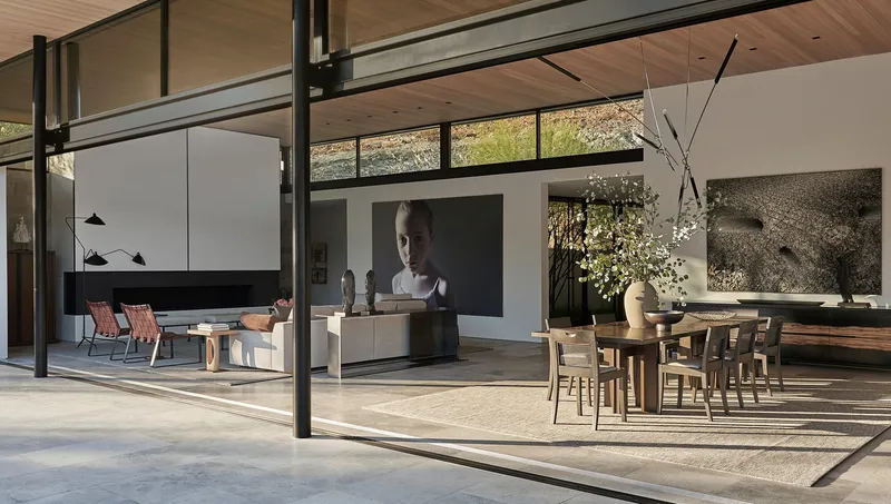 Open-plan living and dining space with steel-framed glass walls and wood ceiling in afternoon light