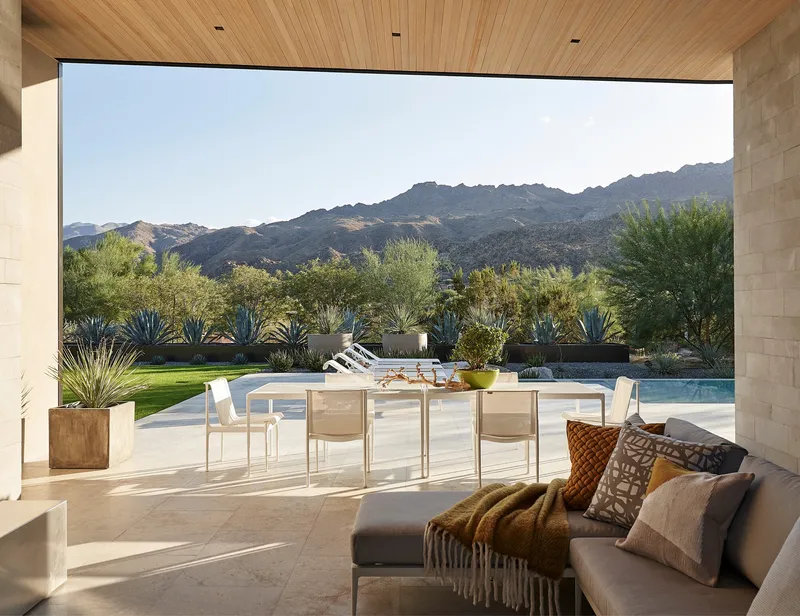 View from interior seating area through wood-clad overhang toward pool and mountain landscape