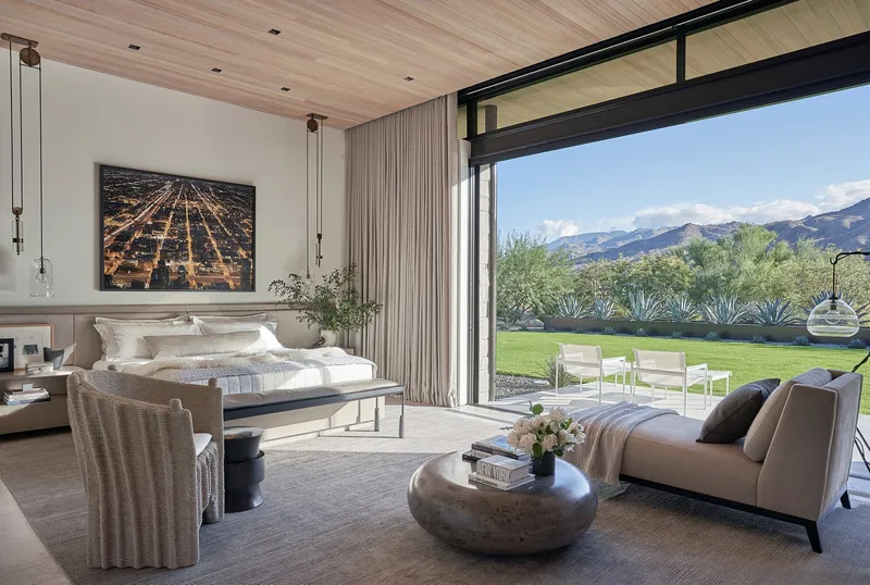 Bedroom with floor-to-ceiling glass doors opening to lawn and desert plantings beyond