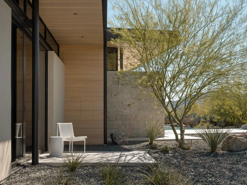 Gravel courtyard with palo verde tree beside limestone-clad wall and wood soffit