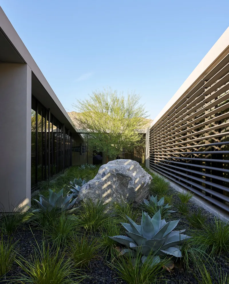 Internal courtyard with large boulder and agave plantings between horizontal louver screen and glazed wall