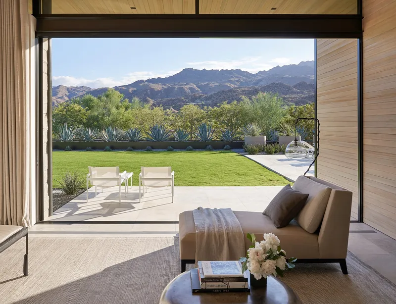 Interior view through sliding glass doors to terrace, lawn, and mountain range beyond