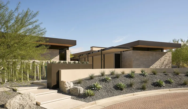 Entry approach showing stucco and stone volumes with cantilevered roofs in desert setting