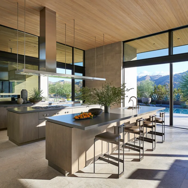 Kitchen with two islands, wood ceiling, and glazed walls facing pool and mountains