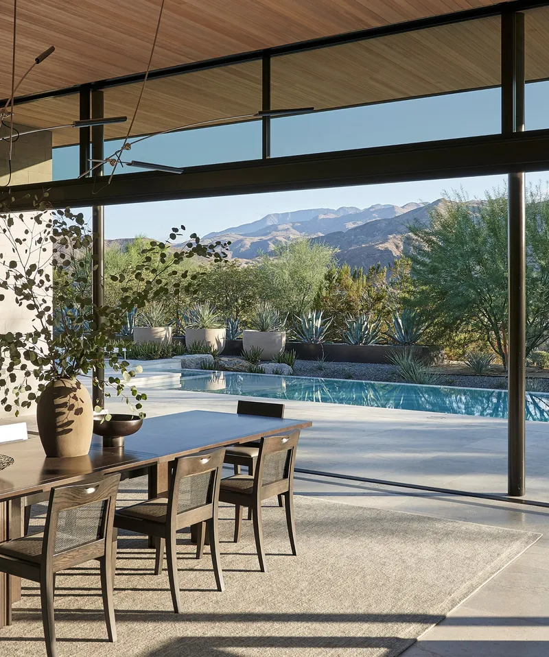 Dining area with timber ceiling looking through glass walls to pool and desert landscape with mountains