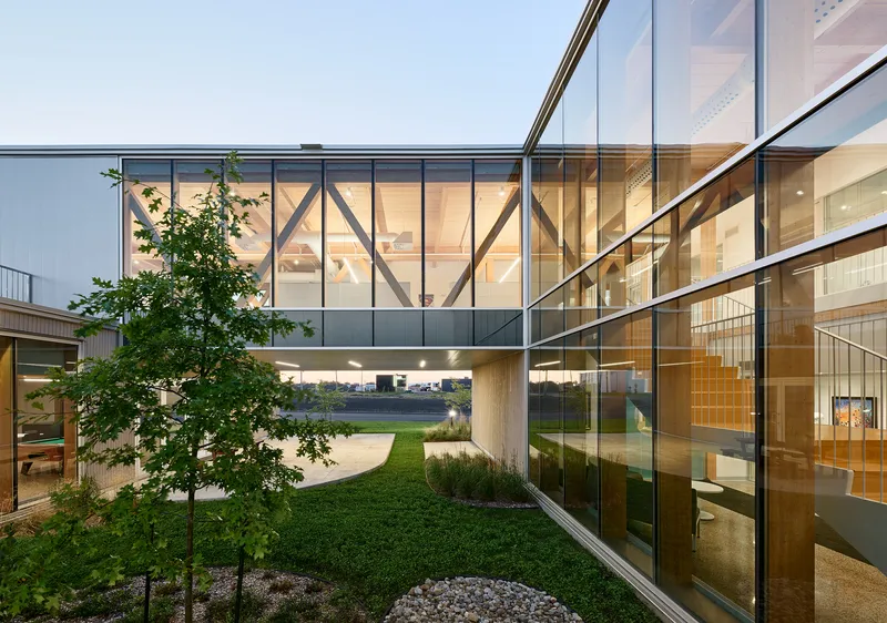 Glazed bridge linking two timber-framed volumes above a landscaped courtyard at twilight