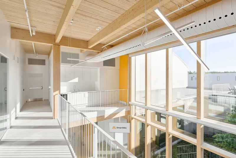 Upper corridor with exposed timber beams and glazed railing overlooking a central atrium