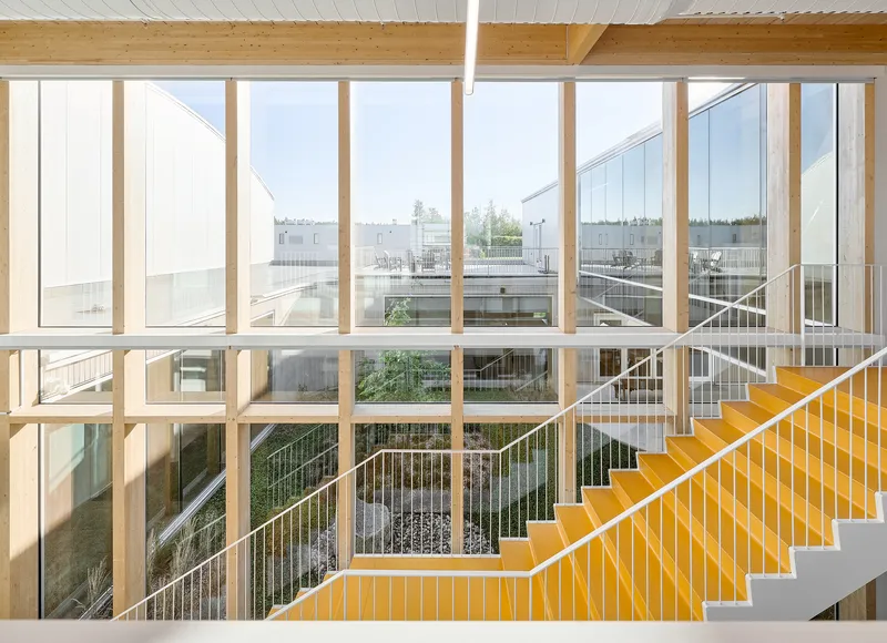 Yellow steel staircase with wire mesh railing framed by floor-to-ceiling timber mullion windows