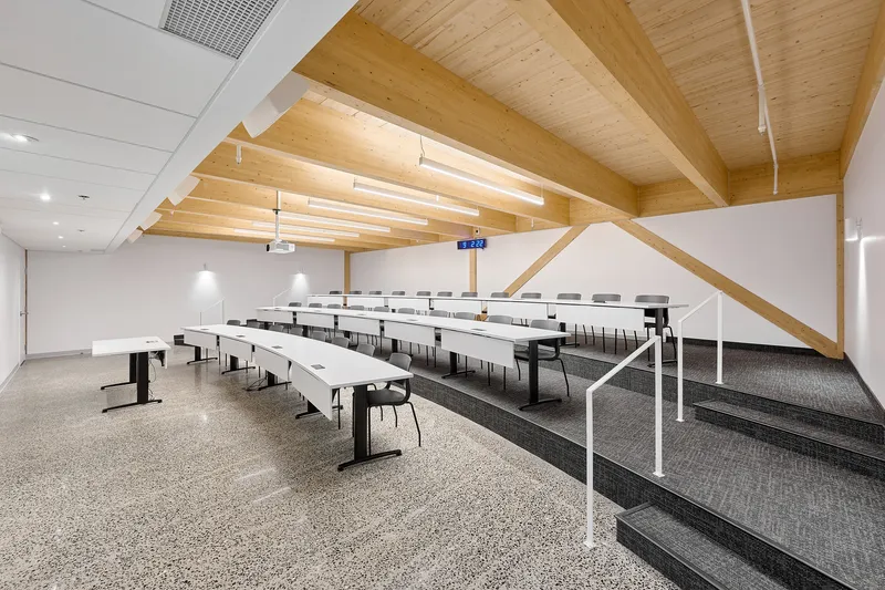 Training room with tiered seating, white tables, and an exposed timber roof structure with vaulted beams