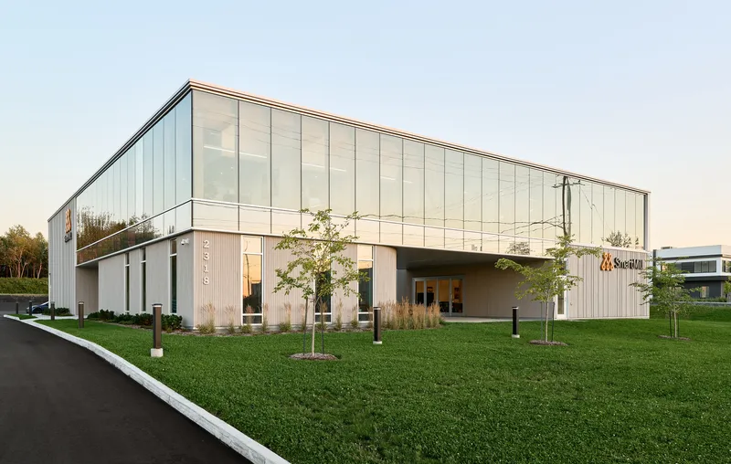 Vertical metal panel and glass facade with young trees planted in a lawn at dusk